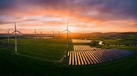 Aerial view of wind turbines and solar panels in rural landscape at golden hour sunset, showcasing renewable energy infrastructure for sustainable power generation.