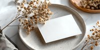 Blank business card on ceramic plate with dried flowers, creating elegant minimalist composition for branding mockup on neutral background.