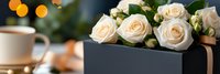 Elegant cream roses in black gift box with coffee cup and warm bokeh lights creating romantic morning atmosphere for special occasions and celebrations.