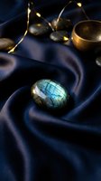 Labradorite gemstone with blue green flash on dark navy silk fabric with golden lights creating mystical atmosphere for jewelry photography and luxury design.