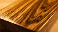 Close-up of polished wood grain with warm golden-brown tones and natural striations, showcasing texture and craftsmanship for furniture, flooring, and interior design projects.