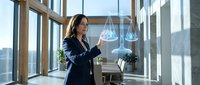 Professional businesswoman in dark suit using tablet in modern office with large windows and city view for corporate technology presentations.