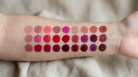 Colorful lipstick swatches on woman's arm showing various pink, red, and berry shades for makeup testing and beauty product comparison purposes.
