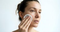 Young Caucasian woman applying skincare product with cotton pad on face during daily beauty routine for healthy glowing skin and facial care regimen.
