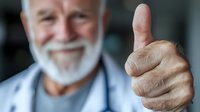Senior Caucasian male with white beard showing thumbs up gesture while smiling. Close-up portrait in light blue medical uniform expressing positivity and approval.