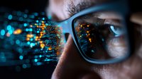 Futuristic digital code reflection in eyeglasses with glowing orange and blue data streams against dark background showing modern technology concept.