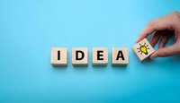 Hand placing wooden cube with lightbulb icon completing word IDEA on blue background representing creativity and innovation in business planning.