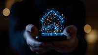 Glowing blue house hologram floating between hands against dark background with bokeh lights, representing smart home technology and digital innovation.