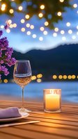 Romantic evening scene with wine glass and candle on wooden table overlooking mountain lake with purple lilac flowers and warm bokeh lights for dining ambiance.