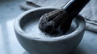 Activated charcoal powder in stone mortar with wooden pestle for natural skincare and detox treatments on marble surface.