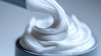 Smooth swirls of white cream forming soft peaks and curves against light background, creating luxurious texture for cosmetic and beauty product advertising.