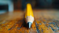 Yellow wooden pencil with sharp graphite tip resting on aged wooden surface with measurement markings for creative writing and artistic projects.