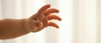 Newborn infant hand reaching out with fingers extended against soft neutral background, symbolizing new life, growth, and parenting concepts.