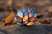 Stained glass lotus flower candle holder in pastel blue and peach colors on stone with autumn leaves, illuminated from within creating magical glow at sunset.