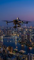 Professional drone with camera flying over illuminated city skyline at dusk for aerial photography and videography projects.