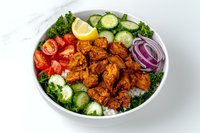 Spicy chicken bowl with fresh vegetables, rice, cucumber slices, cherry tomatoes, red onion rings, and kale garnish served on white plate. Suitable for menu photography.