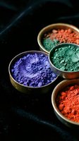 Colorful pigment powders in brass bowls on dark surface. Blue, green, and red mineral pigments for art, cosmetics, and design projects.