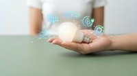 Hand holding glowing light bulb with digital innovation icons representing creative ideas, technology solutions and business inspiration concepts.