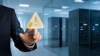 Businessman in dark suit holding glowing warning alert icon in server room environment, representing cybersecurity risk management and system alerts.