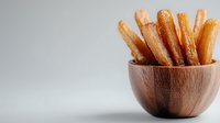 Crispy golden french fries served in wooden bowl against light background, close up view of deep fried potato strips for food service and menu design.