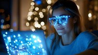Young woman in glowing blue glasses working on laptop at night with bokeh lights background, cybersecurity and digital technology concept.