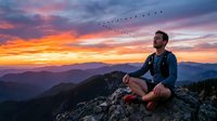 Man sitting on mountain rock at sunset, watching migrating birds fly across colorful sky. Outdoor adventure and nature contemplation scene.