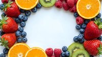 Fresh mixed berries and citrus fruits arranged in circular frame on white background for healthy eating and nutrition concepts.