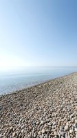 Serene pebble beach with calm turquoise water and clear sky, ideal for travel, relaxation, and coastal resort marketing.