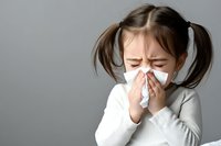 Young girl with pigtails blowing nose into tissue, showing cold or flu symptoms. Child healthcare and seasonal illness concept for medical content.