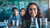 Young Hispanic woman wearing glasses smiles in science laboratory classroom with lab equipment and chalkboard formulas, while classmates work in background.