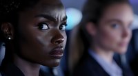 Young African American businesswoman with serious expression in dark office environment, dramatic side lighting highlights determined professional demeanor.