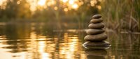 Zen stone stack balanced on water surface during golden hour sunset creating peaceful meditation and mindfulness atmosphere for wellness and spiritual practices.
