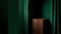 Wooden cube podium display stand against emerald green velvet curtain backdrop for luxury product presentation and branding showcase.
