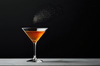 Orange cocktail in martini glass on dark background with splash of salt or sugar powder creating dramatic effect against black backdrop. Perfect for bar menu.
