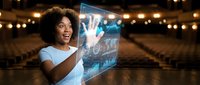 Young African American woman with curly hair wearing light blue shirt interacting with glowing holographic display screen in modern auditorium setting for technology and innovation concepts.