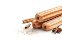Churros with cinnamon powder, star anise and cinnamon sticks on white background, traditional Spanish dessert isolated for food photography and menu design.