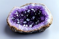 Natural amethyst geode with deep purple crystals and rough exterior surface isolated on white background for jewelry and mineral collection designs.