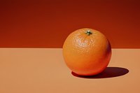 Fresh ripe orange on a warm orange-toned background with dramatic shadow, minimalist studio composition for food and healthy lifestyle concepts.