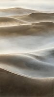 Windswept sand dunes with flowing mist creating ethereal desert landscape in soft golden light for nature and travel backgrounds.