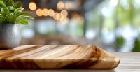 Wooden serving board with natural grain pattern on kitchen counter with decorative plant and blurred bokeh background. Modern minimalist food presentation.