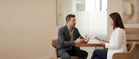 Mature man in business casual attire and woman in professional white blouse having discussion in modern office setting, suitable for corporate training and workplace communication concepts.