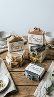 Handmade natural soaps with botanical labels stacked on wooden surface, featuring lavender, wild rose, sea salt varieties for spa, wellness, and organic beauty product marketing.