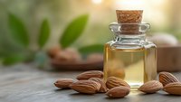 Golden almond oil in glass bottle with cork stopper surrounded by raw almonds on wooden surface with blurred green leaves background for skincare.