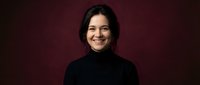 Young Hispanic woman smiling warmly in black turtleneck against burgundy background for professional headshot and portrait photography.