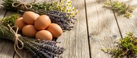 Fresh brown eggs nestled with dried lavender bundles and wildflowers on rustic wooden planks creating farmhouse kitchen aesthetic for cooking blogs.