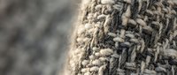 Close-up macro shot of natural woven textile fabric showing detailed fiber texture and intricate weave pattern in neutral beige and brown tones.