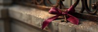 Vintage brass key tied with burgundy velvet ribbon rests on weathered wooden surface with soft bokeh background, creating nostalgic romantic atmosphere.