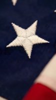 White embroidered star on navy blue fabric with red and white stripes, close-up detail of American flag textile for patriotic designs and Memorial Day projects.