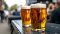 Fresh craft beer glasses with golden foam on outdoor terrace table. Refreshing alcoholic beverages for social gathering and relaxation moments.