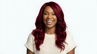 Young African American woman with burgundy red wavy hair laughing joyfully in casual white ribbed top against light background for lifestyle content.